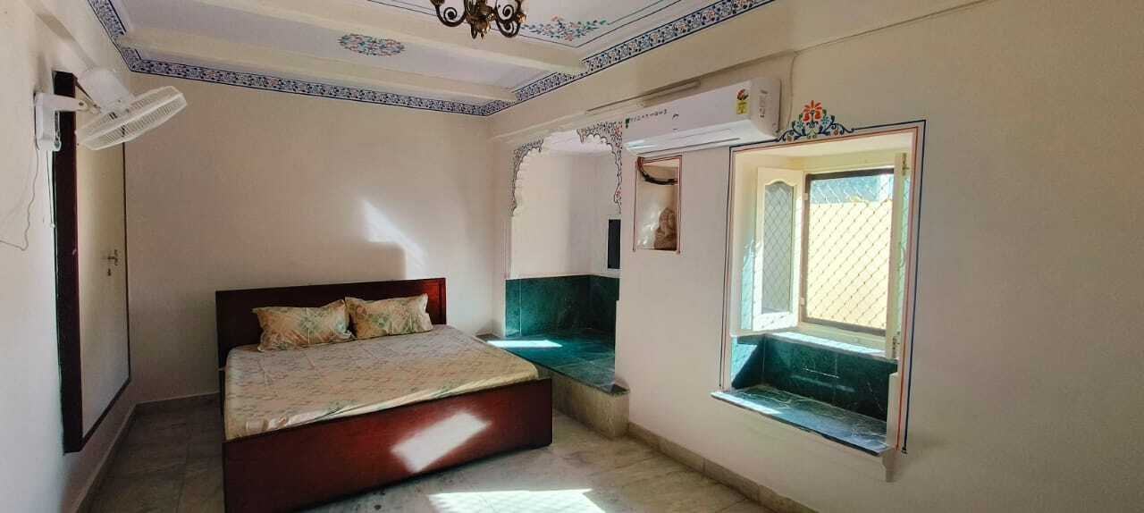 Traditional bedroom with wooden double bed, cushioned window seating, marble flooring, and decorative ceiling design